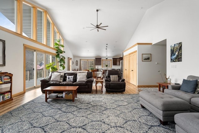 living room featuring a towering ceiling, light wood-style floors, and ceiling fan