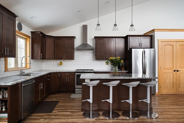 kitchen with dark brown cabinetry, appliances with stainless steel finishes, vaulted ceiling, wall chimney range hood, and a sink