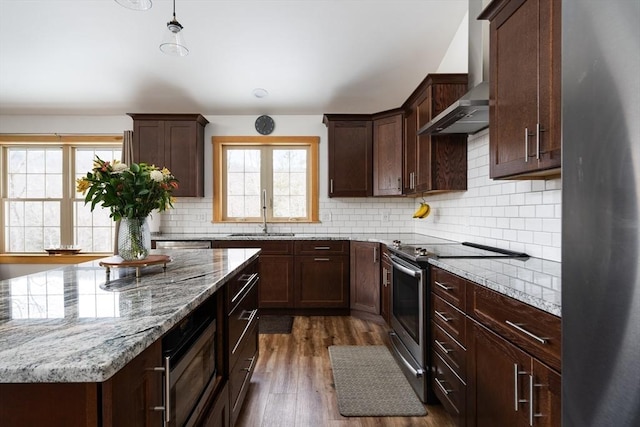 kitchen featuring tasteful backsplash, wall chimney exhaust hood, appliances with stainless steel finishes, dark wood-type flooring, and a sink