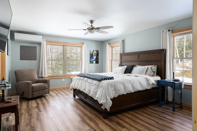 bedroom with a ceiling fan, baseboards, an AC wall unit, and wood finished floors