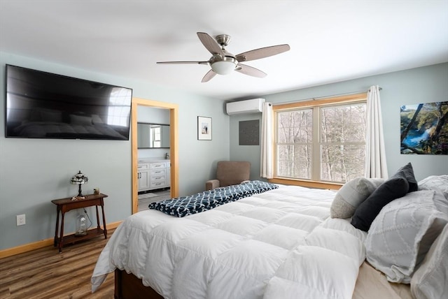 bedroom with a wall unit AC, ensuite bathroom, a ceiling fan, wood finished floors, and baseboards