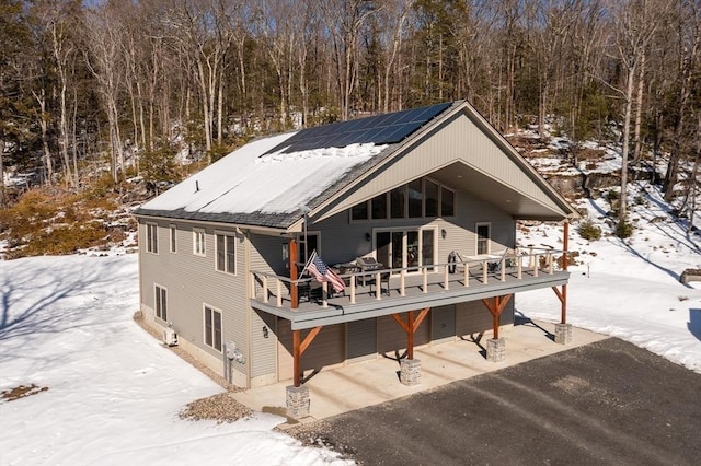 view of front of house featuring driveway, solar panels, an attached garage, a deck, and a wooded view