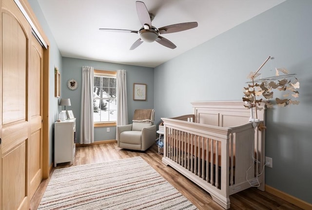 bedroom featuring a closet, a crib, baseboards, and wood finished floors