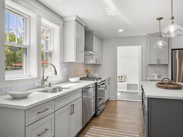 kitchen with appliances with stainless steel finishes, a sink, light countertops, decorative light fixtures, and tasteful backsplash
