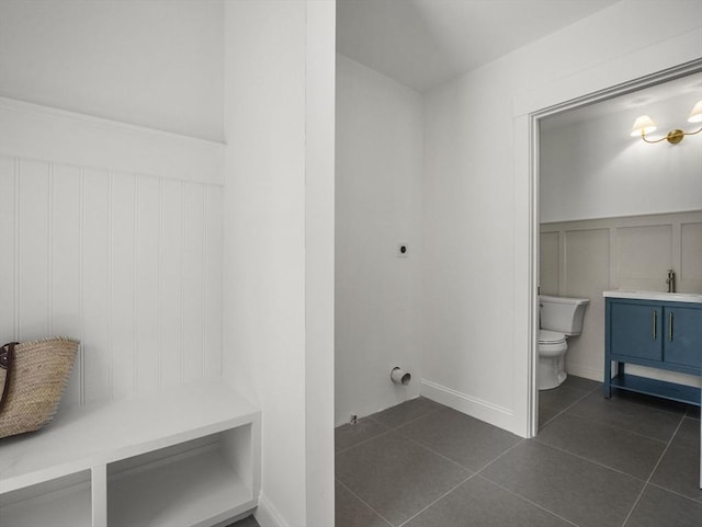 laundry area with laundry area, a decorative wall, a wainscoted wall, dark tile patterned floors, and hookup for an electric dryer