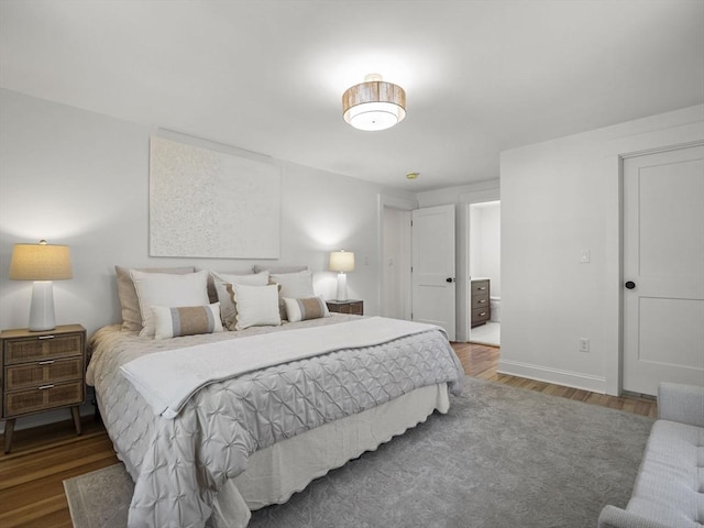 bedroom featuring baseboards, wood finished floors, and ensuite bath