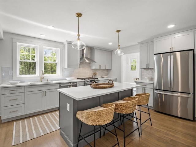 kitchen with backsplash, appliances with stainless steel finishes, a sink, light countertops, and wall chimney exhaust hood