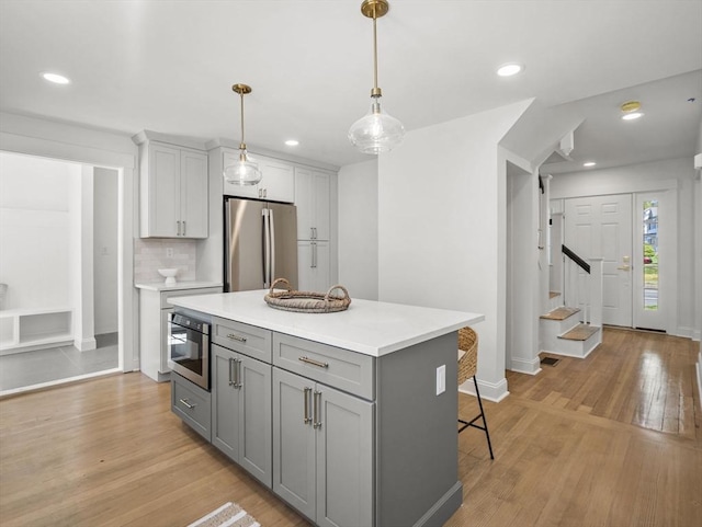 kitchen featuring light countertops, light wood-style flooring, freestanding refrigerator, a kitchen island, and gray cabinetry