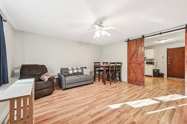 living room with ceiling fan, a barn door, and light hardwood / wood-style floors