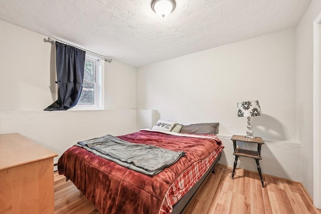 bedroom with light hardwood / wood-style floors, a textured ceiling, and a baseboard radiator