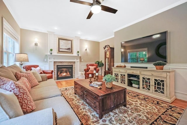 living room with ornamental molding, ceiling fan, wood finished floors, a fireplace, and wainscoting
