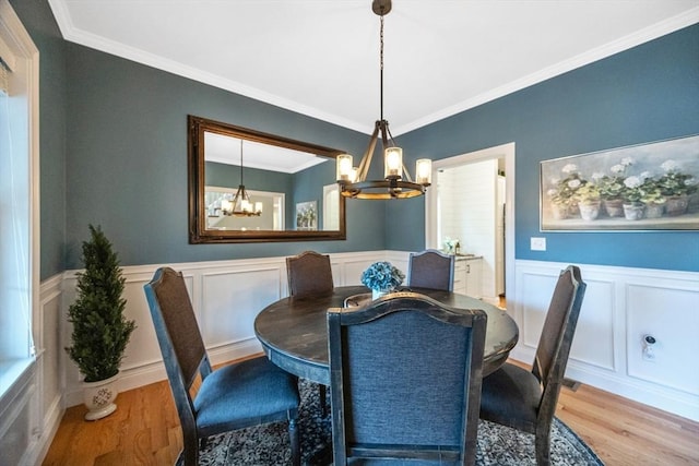 dining room with a chandelier, wood finished floors, a decorative wall, ornamental molding, and a wainscoted wall