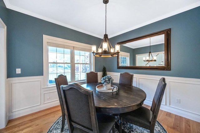 dining space featuring a chandelier, light wood-type flooring, wainscoting, crown molding, and a decorative wall