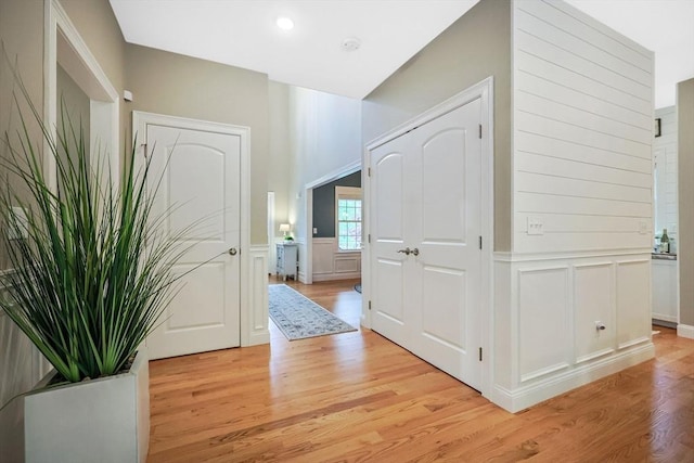 corridor with a decorative wall, light wood finished floors, and wainscoting