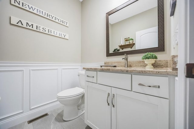 half bathroom with toilet, vanity, wainscoting, and a decorative wall