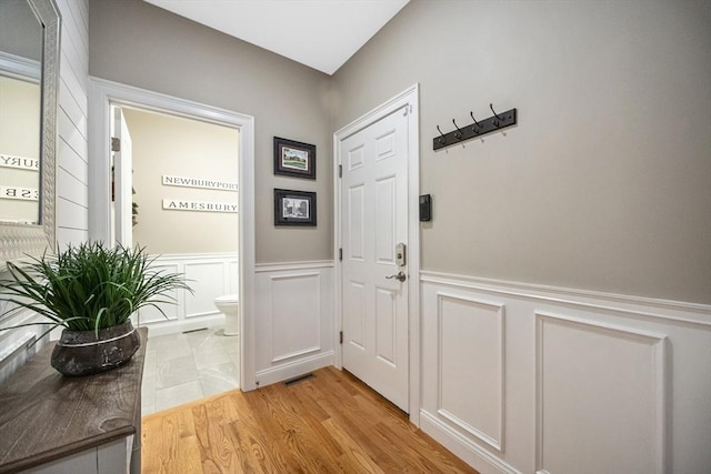 entryway with a decorative wall, wainscoting, and light wood-type flooring