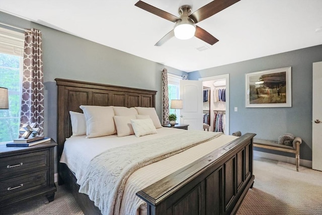 bedroom featuring carpet, multiple windows, a spacious closet, and a ceiling fan