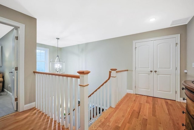 hall with an upstairs landing, light wood-type flooring, and baseboards