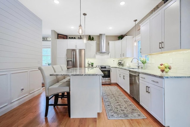kitchen featuring appliances with stainless steel finishes, wall chimney exhaust hood, a sink, decorative backsplash, and light stone countertops