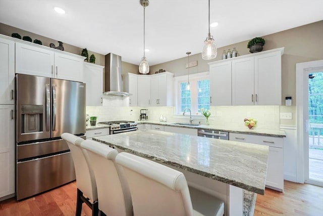 kitchen with stainless steel appliances, wall chimney exhaust hood, a sink, plenty of natural light, and recessed lighting