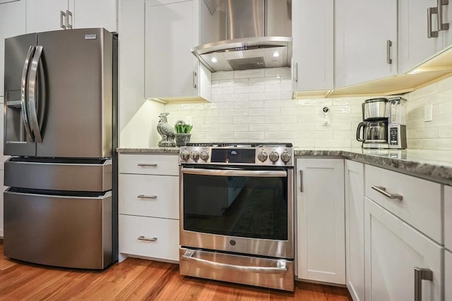 kitchen featuring appliances with stainless steel finishes, wall chimney exhaust hood, light wood finished floors, white cabinets, and light stone counters