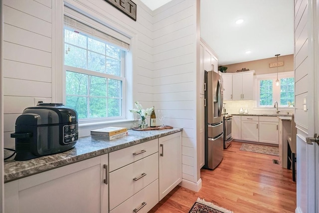 kitchen featuring appliances with stainless steel finishes, light wood-style floors, white cabinetry, and light stone counters