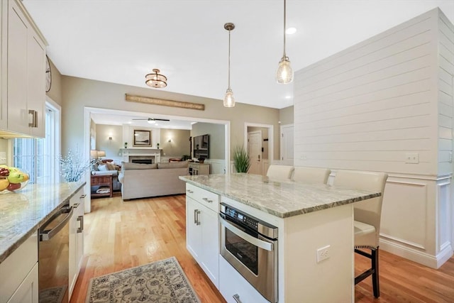 kitchen with stainless steel appliances, light wood-style floors, a kitchen breakfast bar, a fireplace, and recessed lighting