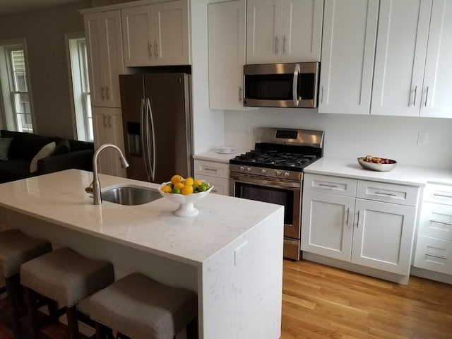 kitchen with appliances with stainless steel finishes, light stone counters, light hardwood / wood-style floors, white cabinets, and sink