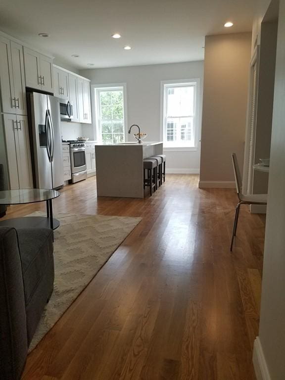 kitchen with light hardwood / wood-style floors, white cabinets, a center island with sink, stainless steel appliances, and a kitchen breakfast bar