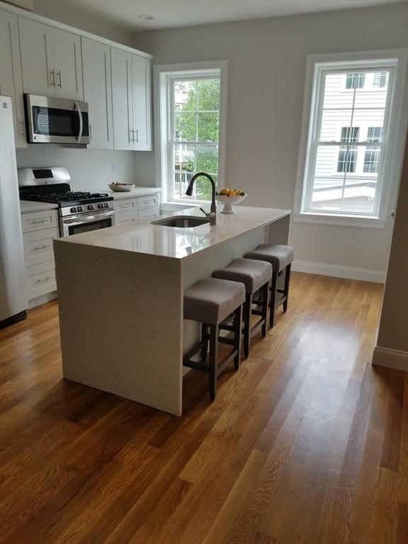 kitchen featuring appliances with stainless steel finishes, light hardwood / wood-style floors, white cabinetry, a kitchen bar, and sink