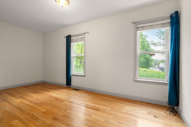 empty room featuring plenty of natural light, baseboards, and light wood-style floors