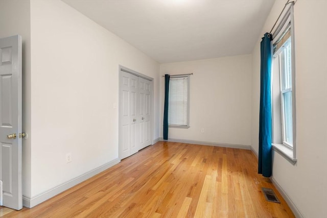 unfurnished bedroom featuring multiple windows, baseboards, visible vents, and light wood-style floors