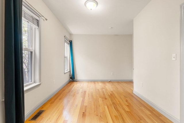 spare room with light wood finished floors, visible vents, and baseboards