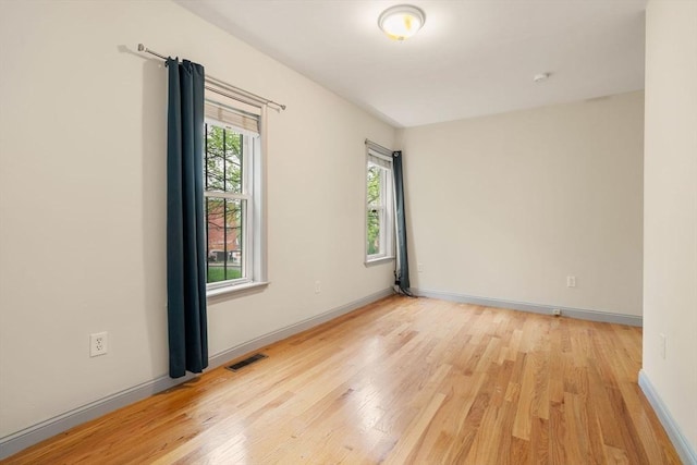 empty room featuring light wood finished floors, visible vents, and baseboards