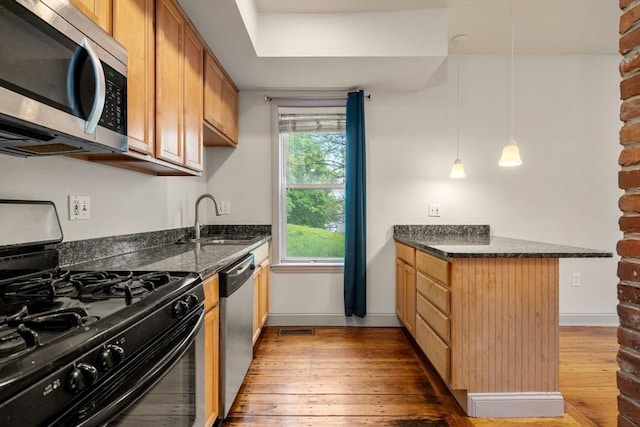 kitchen with a sink, a peninsula, hardwood / wood-style flooring, and appliances with stainless steel finishes