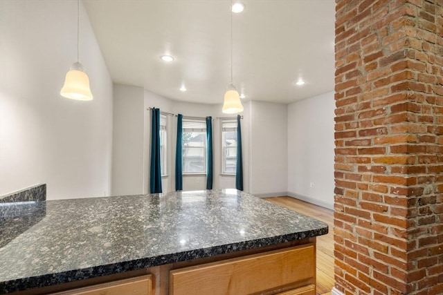 kitchen with light wood-style flooring, dark stone countertops, and decorative light fixtures