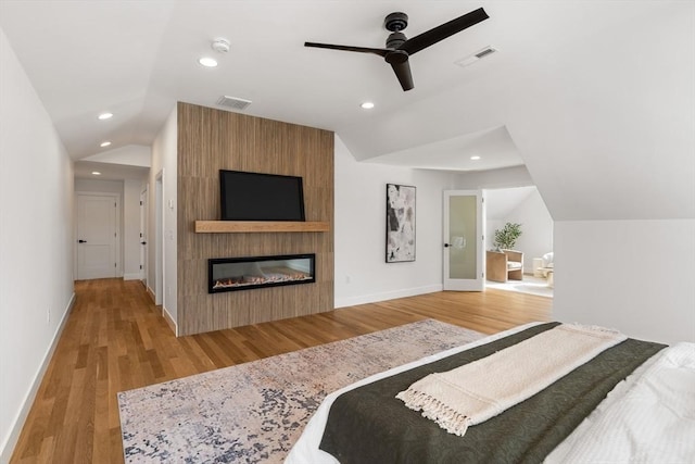 bedroom featuring vaulted ceiling, ceiling fan, a fireplace, and light hardwood / wood-style flooring