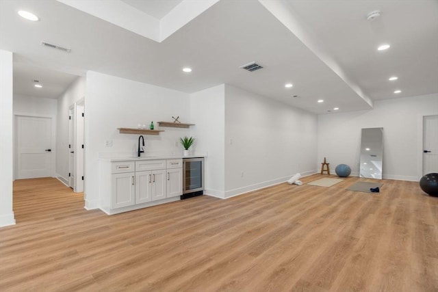 exercise area featuring indoor wet bar, beverage cooler, and light hardwood / wood-style flooring