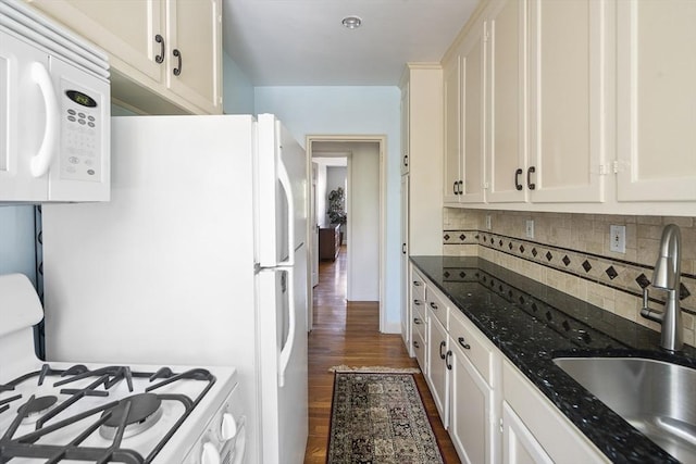 kitchen with a sink, white appliances, white cabinetry, backsplash, and dark wood-style floors