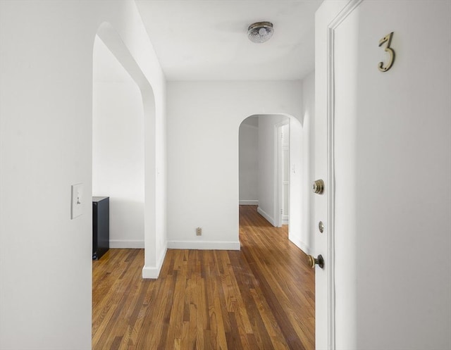 corridor featuring wood finished floors, baseboards, and arched walkways