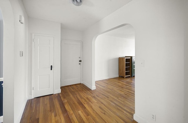 foyer entrance with wood finished floors, baseboards, and arched walkways