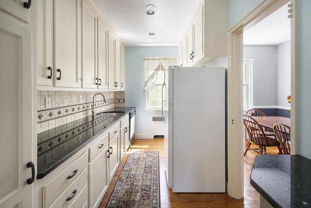 kitchen with a sink, tasteful backsplash, dark stone countertops, freestanding refrigerator, and white cabinets