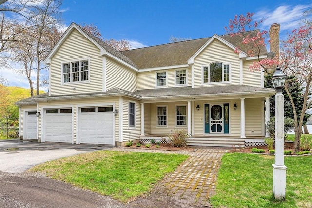 view of front of property with a porch, a garage, driveway, a front lawn, and a chimney