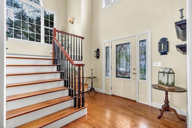 foyer featuring healthy amount of natural light, stairs, wood finished floors, a towering ceiling, and baseboards
