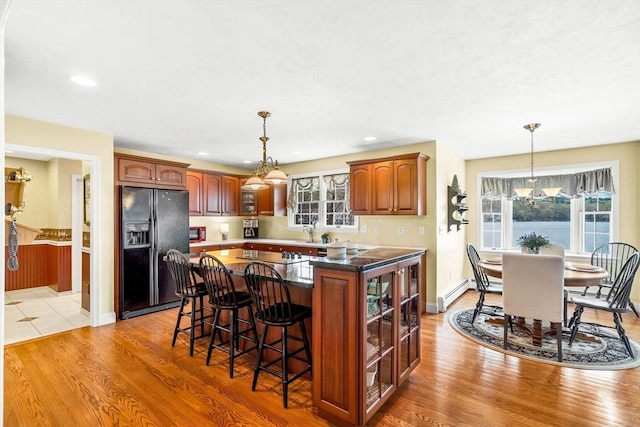 kitchen with black appliances, glass insert cabinets, a center island, a breakfast bar, and hanging light fixtures