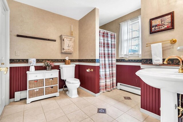 full bathroom with a baseboard heating unit, a wainscoted wall, toilet, tile patterned floors, and a shower with shower curtain
