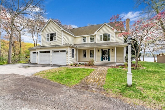 view of front of property featuring an attached garage, driveway, a porch, a chimney, and a front yard