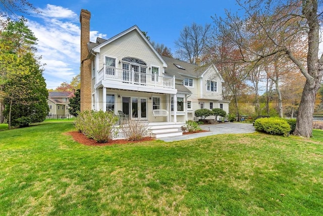 rear view of property with a balcony, a chimney, and a yard