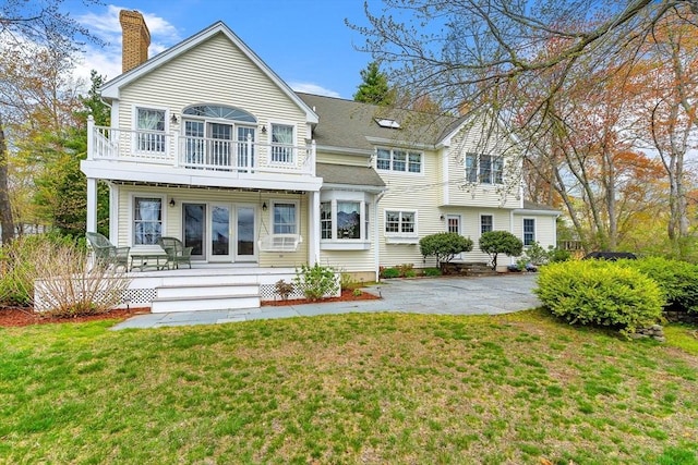 rear view of house with a balcony, a chimney, a yard, and french doors
