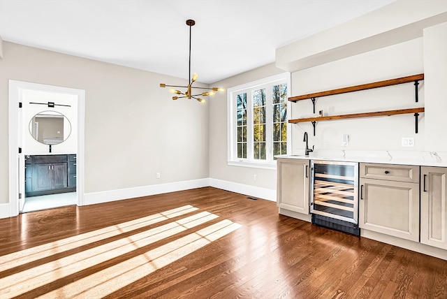 bar featuring dark wood-type flooring, an inviting chandelier, wine cooler, light stone countertops, and decorative light fixtures